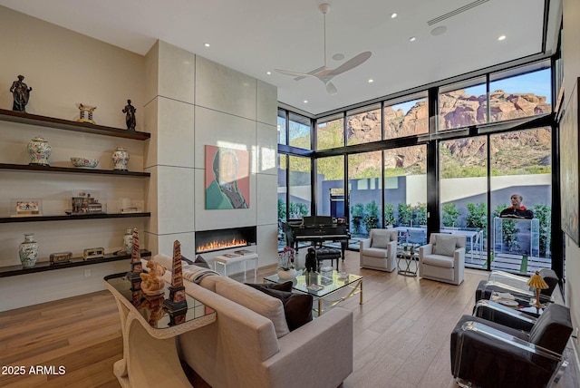 living area with a tile fireplace, floor to ceiling windows, light wood-style flooring, and a high ceiling