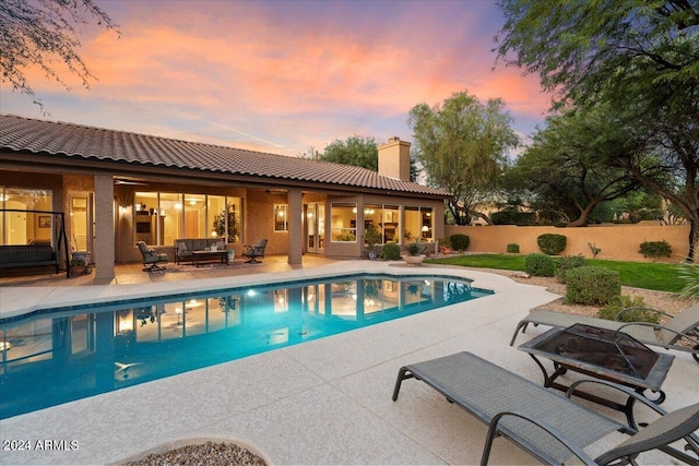 pool at dusk with outdoor lounge area and a patio