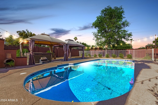 pool at dusk featuring a gazebo, a patio, and a hot tub