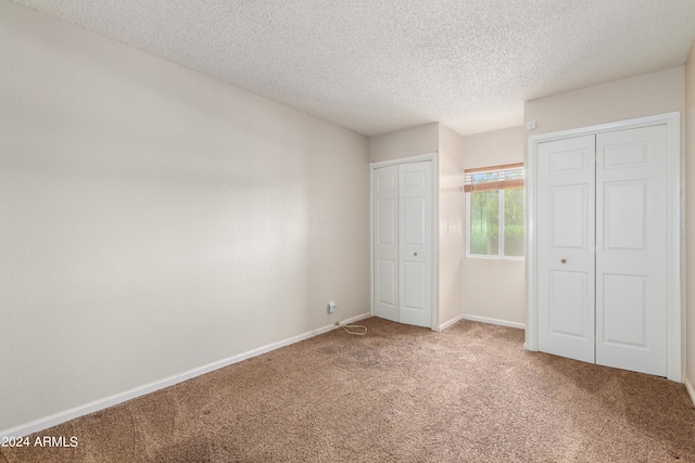 unfurnished bedroom featuring two closets, carpet, and a textured ceiling