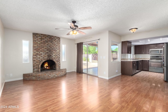 unfurnished living room featuring ceiling fan, sink, a brick fireplace, a textured ceiling, and light wood-type flooring