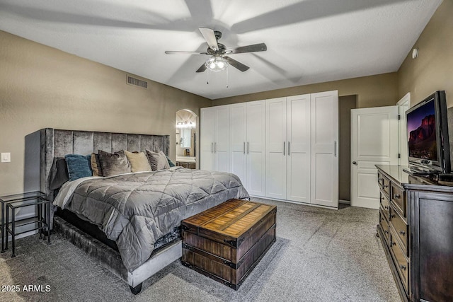 bedroom featuring ceiling fan, ensuite bathroom, and dark carpet