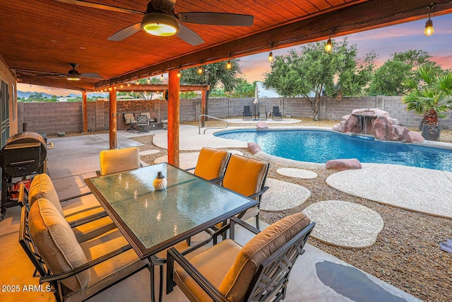 pool at dusk featuring pool water feature, ceiling fan, and a patio area