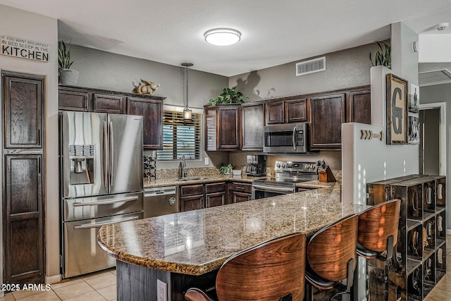 kitchen with appliances with stainless steel finishes, light stone countertops, sink, and dark brown cabinets