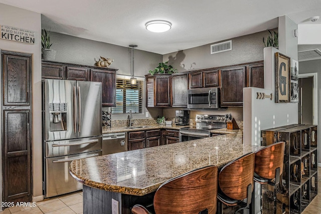 kitchen with light stone counters, appliances with stainless steel finishes, sink, and dark brown cabinets