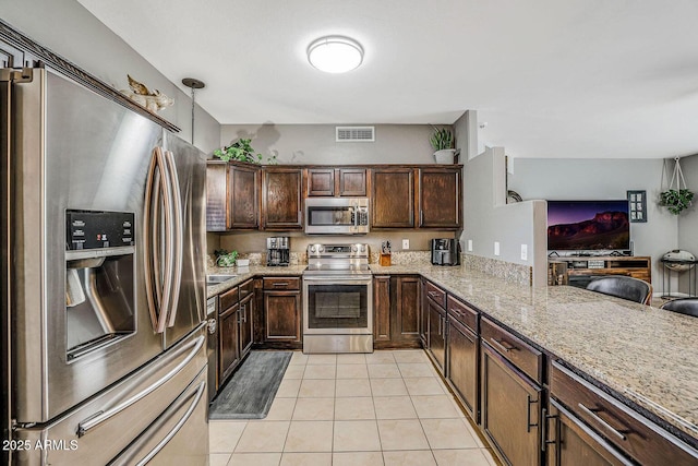 kitchen with light tile patterned flooring, kitchen peninsula, pendant lighting, stainless steel appliances, and light stone countertops