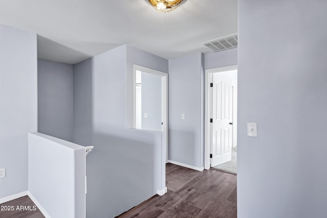 hallway with an upstairs landing, visible vents, baseboards, and wood finished floors