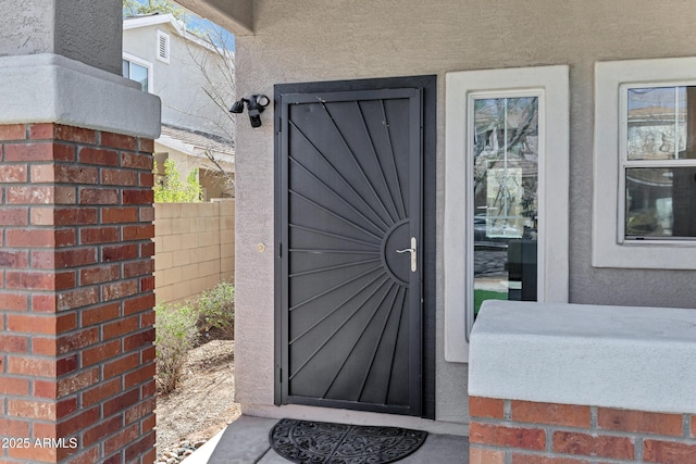 view of exterior entry featuring fence and stucco siding