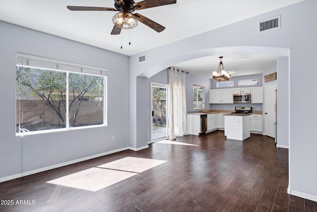 unfurnished living room with visible vents, baseboards, dark wood-style flooring, arched walkways, and a sink