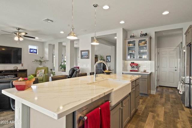 kitchen featuring a center island with sink, glass insert cabinets, open floor plan, and a sink