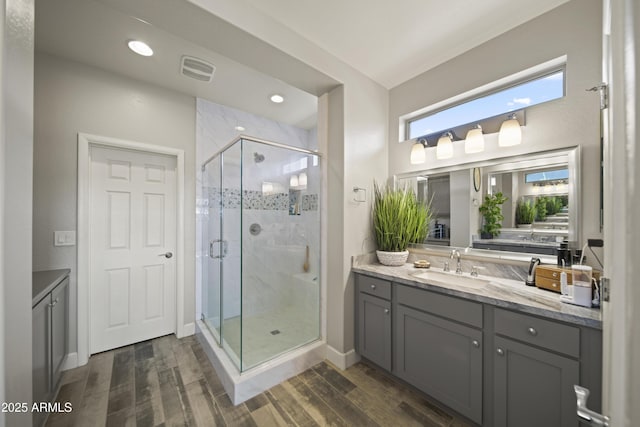 full bath featuring wood finished floors, visible vents, vanity, baseboards, and a stall shower