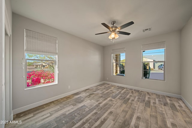 empty room featuring a ceiling fan, wood finished floors, visible vents, and baseboards