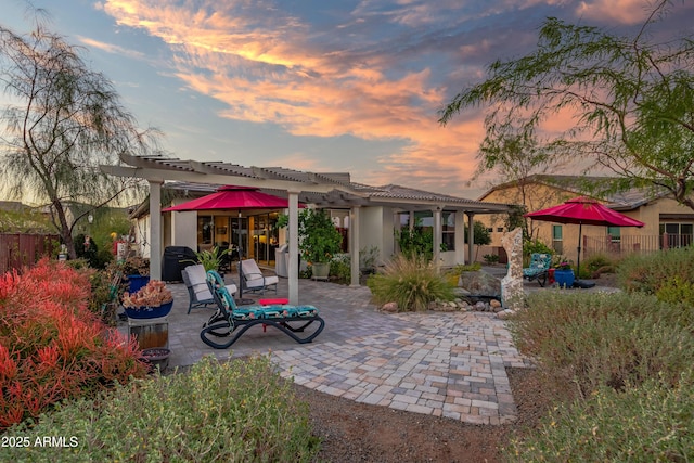 back of property at dusk featuring stucco siding, a patio area, fence, and a pergola