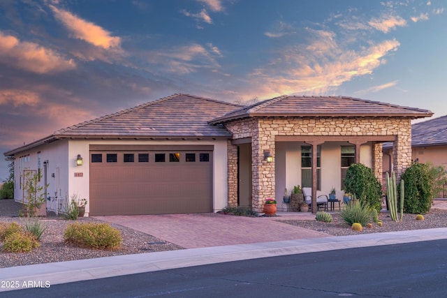 view of front facade featuring a garage, stone siding, decorative driveway, and stucco siding