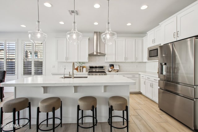 kitchen with decorative light fixtures, stainless steel appliances, wall chimney exhaust hood, and white cabinets