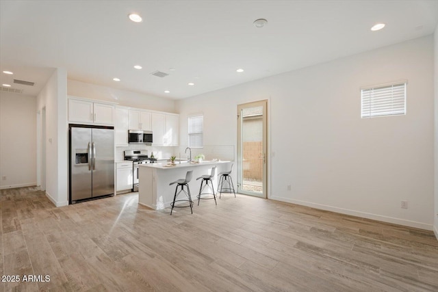 kitchen with stainless steel appliances, plenty of natural light, a kitchen bar, a center island with sink, and white cabinets