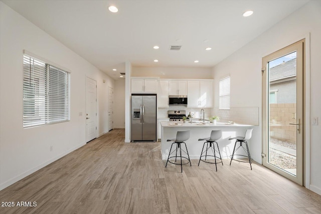 kitchen with white cabinetry, appliances with stainless steel finishes, light hardwood / wood-style floors, kitchen peninsula, and a breakfast bar area