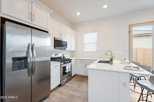 kitchen with sink, stainless steel appliances, kitchen peninsula, plenty of natural light, and white cabinets