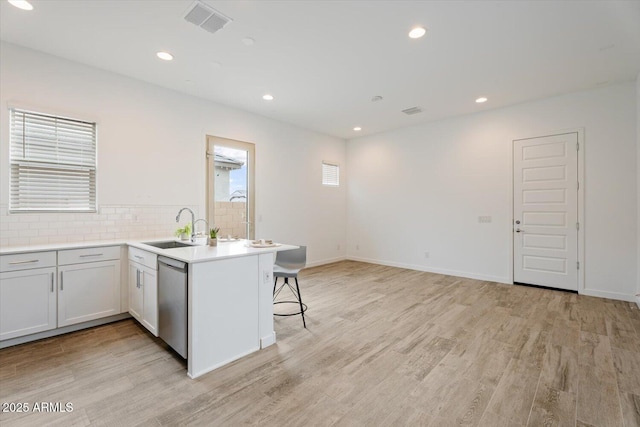 kitchen with a kitchen bar, kitchen peninsula, sink, dishwasher, and light hardwood / wood-style floors