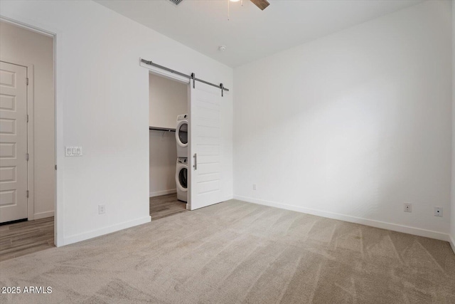 unfurnished bedroom with ceiling fan, a barn door, a spacious closet, stacked washer / drying machine, and light colored carpet