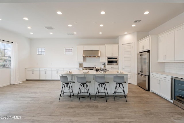 kitchen with white cabinets, beverage cooler, an island with sink, and appliances with stainless steel finishes