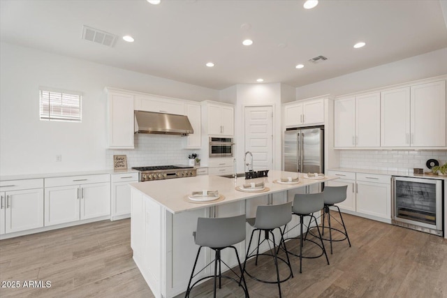 kitchen with stainless steel appliances, sink, white cabinetry, a center island with sink, and wine cooler