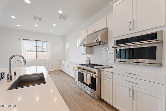 kitchen featuring light stone countertops, appliances with stainless steel finishes, sink, white cabinets, and range hood