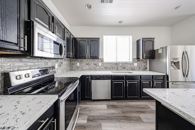 15365 W Valentine St, Surprise, AZ 85379 - kitchen featuring appliances with stainless steel finishes, a sink, dark cabinetry, tasteful backsplash, and light wood-style floors