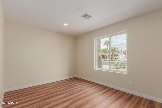 empty room with baseboards, visible vents, and light wood finished floors