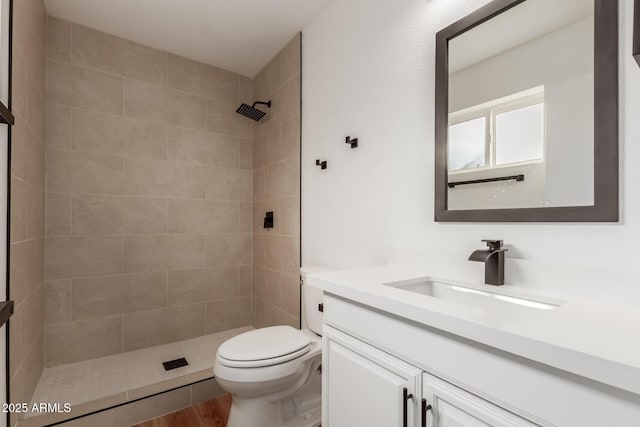 bathroom with tiled shower, toilet, wood finished floors, and vanity