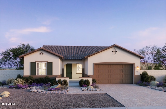 mediterranean / spanish-style home with decorative driveway, a tile roof, stucco siding, an attached garage, and fence