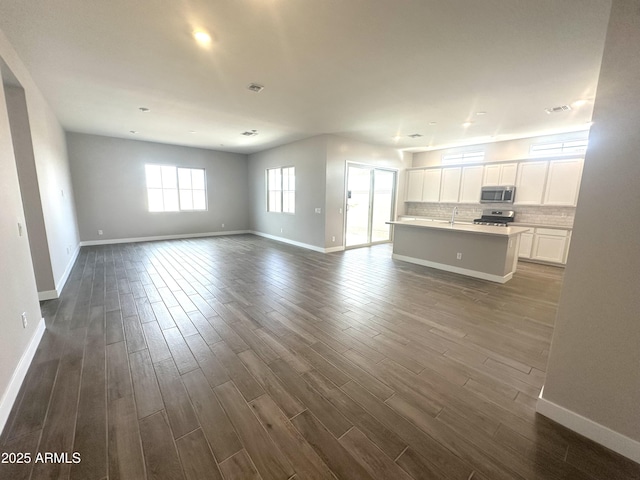 unfurnished living room featuring dark wood-style flooring, visible vents, and baseboards