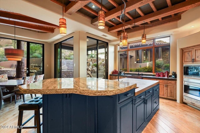 kitchen featuring light hardwood / wood-style flooring, a kitchen island, beamed ceiling, appliances with stainless steel finishes, and pendant lighting