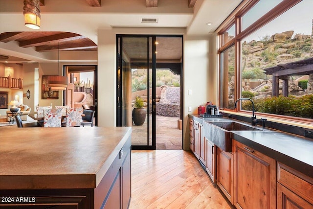 kitchen with beamed ceiling, sink, light hardwood / wood-style flooring, and decorative light fixtures