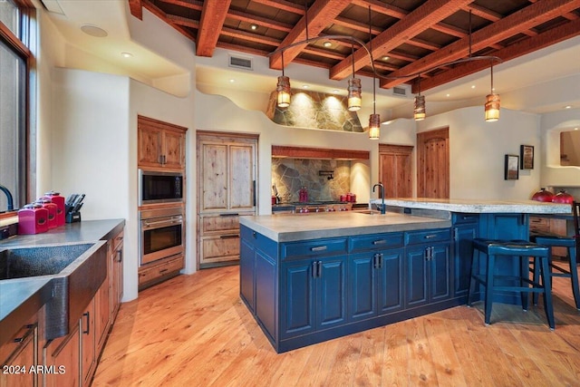 kitchen with light hardwood / wood-style floors, black microwave, an island with sink, a breakfast bar area, and oven