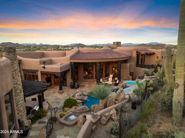 back house at dusk with a patio, a mountain view, and a fenced in pool