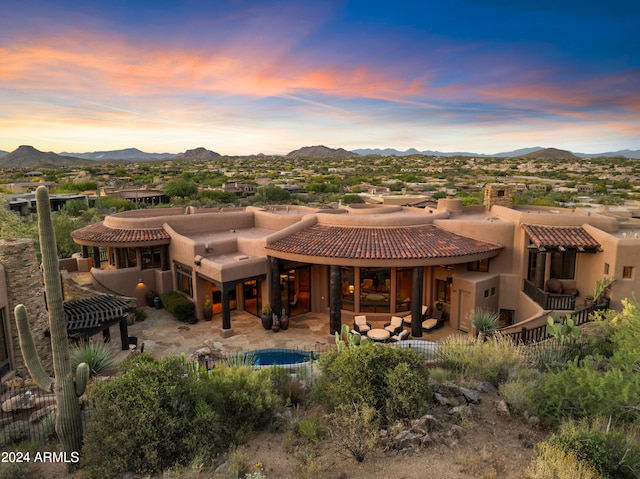 back house at dusk with a patio, a mountain view, and a fenced in pool