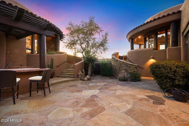 patio terrace at dusk featuring a pergola and exterior bar