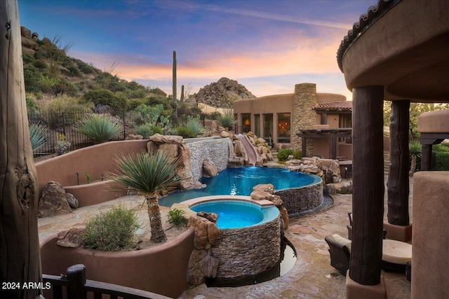 pool at dusk featuring an in ground hot tub and a water slide