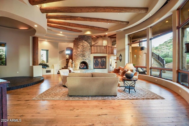 living room featuring ceiling fan, a stone fireplace, high vaulted ceiling, wood-type flooring, and beamed ceiling