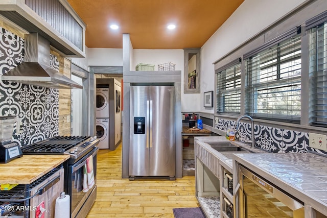 816 Tombstone Cyn Unit C, Bisbee, AZ 85603 - kitchen with appliances with stainless steel finishes, stacked washer / dryer, tile countertops, light wood-type flooring, and extractor fan