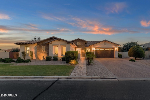 mediterranean / spanish house with stucco siding, decorative driveway, stone siding, fence, and an attached garage