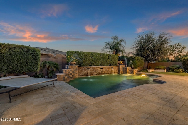 pool at dusk featuring a fenced backyard, an outdoor kitchen, and a patio