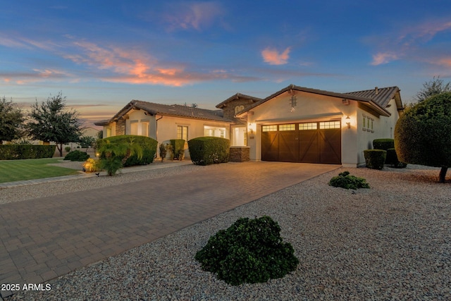 mediterranean / spanish-style home with stucco siding, a tiled roof, decorative driveway, and a garage