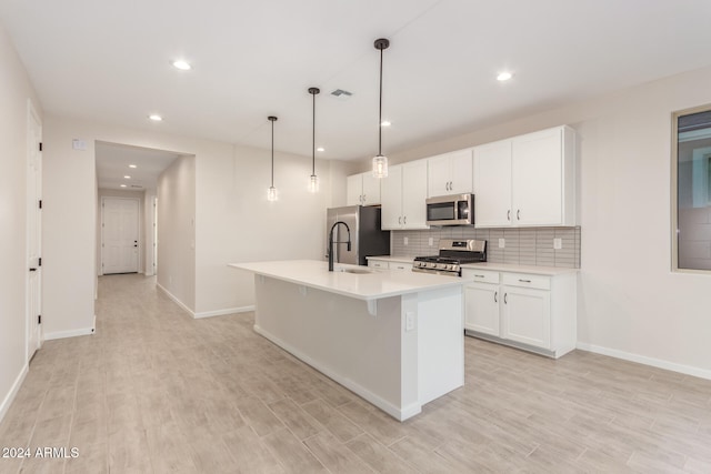 kitchen featuring a kitchen island with sink, white cabinets, light hardwood / wood-style flooring, decorative light fixtures, and stainless steel appliances