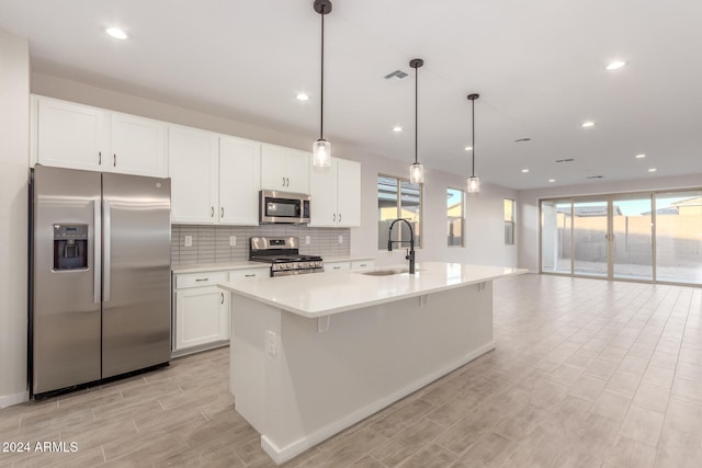 kitchen with white cabinetry, sink, pendant lighting, a kitchen island with sink, and appliances with stainless steel finishes