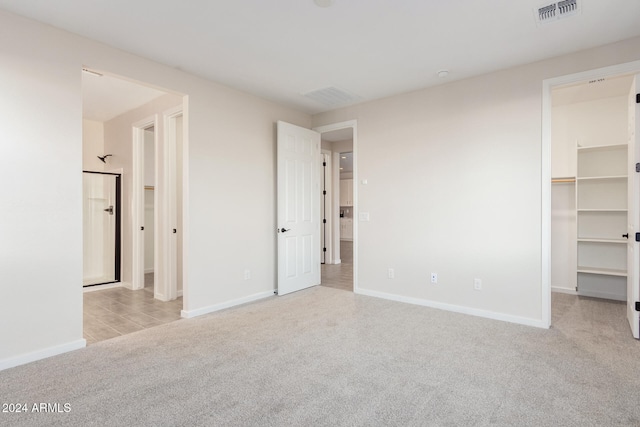 unfurnished bedroom with a walk in closet, a closet, and light colored carpet