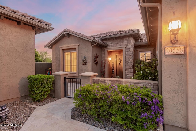 20558 N 263rd Dr, Buckeye, AZ 85396 - doorway to property featuring a tile roof, a gate, fence, stone siding, and stucco siding