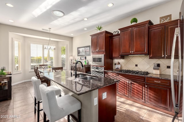 kitchen with backsplash, a sink, light tile patterned floors, reddish brown cabinets, and stainless steel appliances