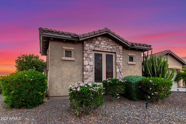 view of front facade with a tiled roof, stone siding, and stucco siding